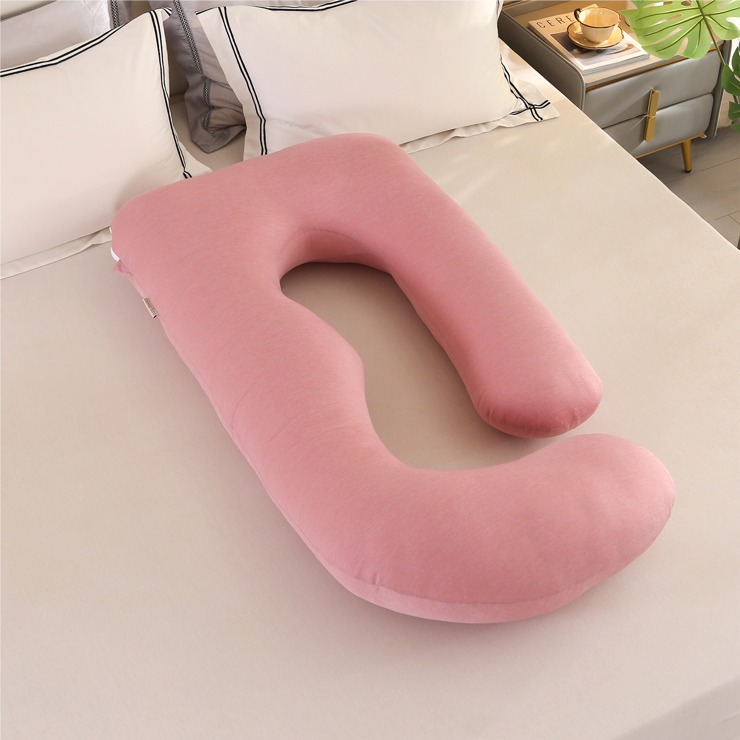 Blush Pink J Pregnancy Pillow with cooling cover on a bed